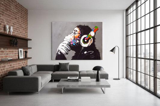 Large colorful chimpanzee painting with headphones displayed above a gray sectional sofa in a modern living room with brick accents and city‑view windows.