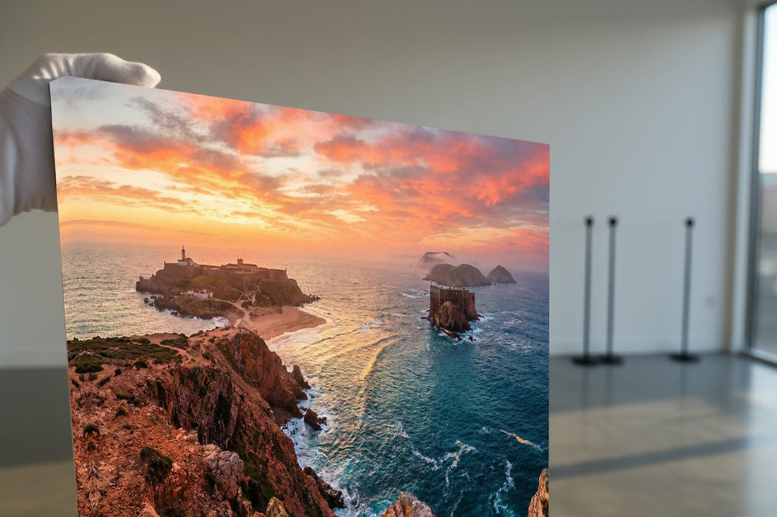 arge sunset coastal photograph showing rugged cliffs, a sandy beach, and a fortress on a rocky headland, held by a gloved hand during inspection.