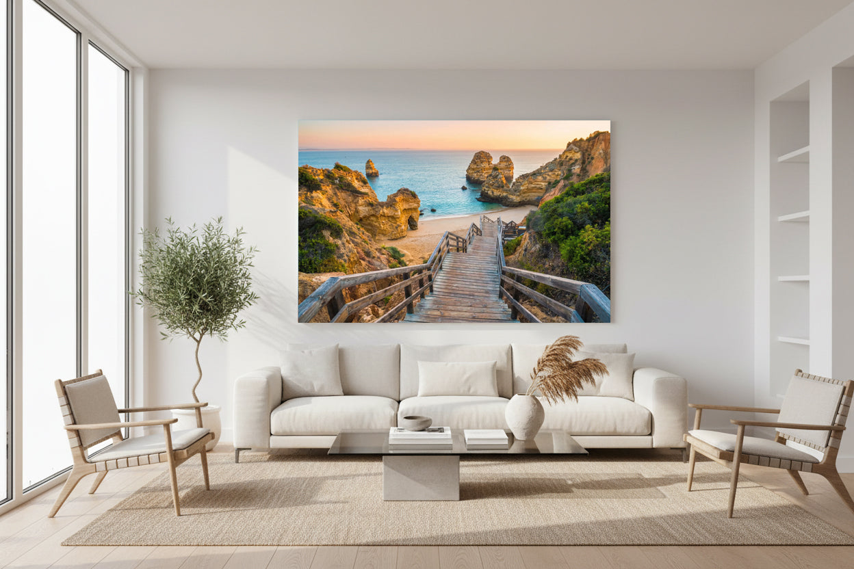 “Large coastal sunset canvas showing a wooden staircase leading to a beach, displayed in a modern minimalist living room with neutral décor and natural light.”
