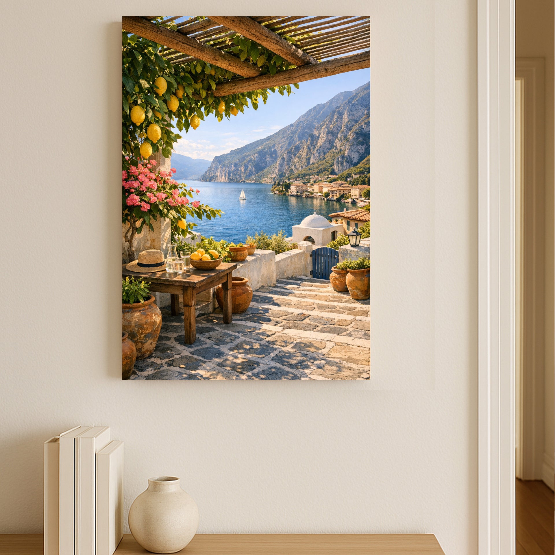 Framed artwork of a scenic view with a lake, mountains, and a table with fruit on a white wall.