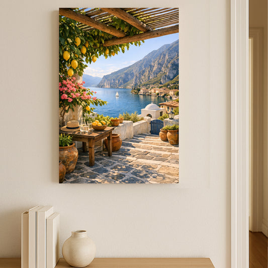 Framed artwork of a scenic view with a lake, mountains, and a table with fruit on a white wall.