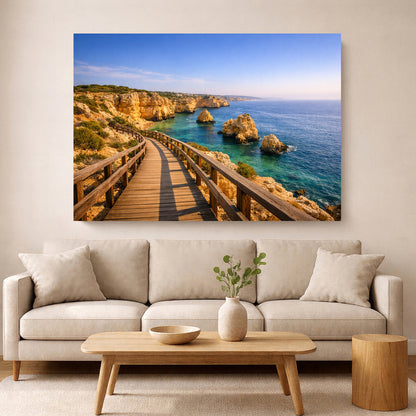 A large rectangular wall art print showing a coastal rocky sea with a wooden boardwalk, displayed above a light beige sofa in a modern living room setting - Portugal Canvas Co