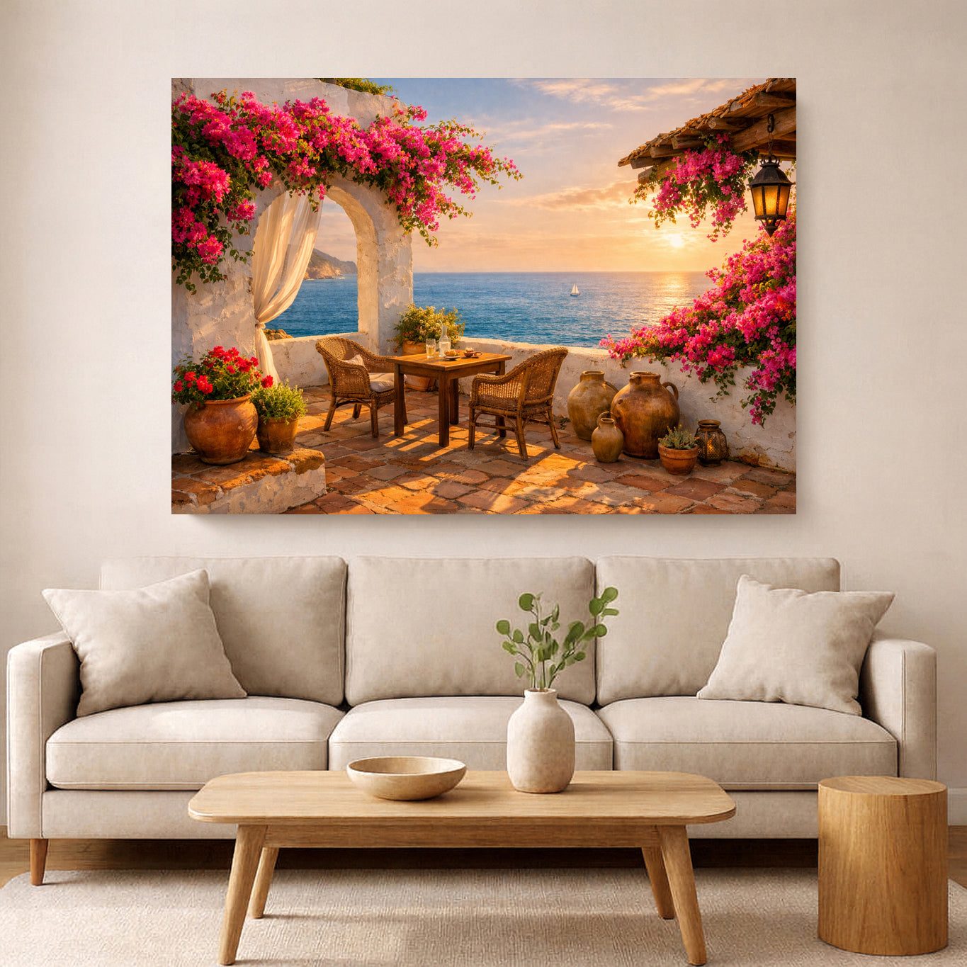 A large rectangular wall art print depicting a Mediterranean seaside patio with pink bougainvillea flowers, a table and chairs, terracotta pots, and a sunset over the ocean, displayed above a light beige sofa in a modern living room.