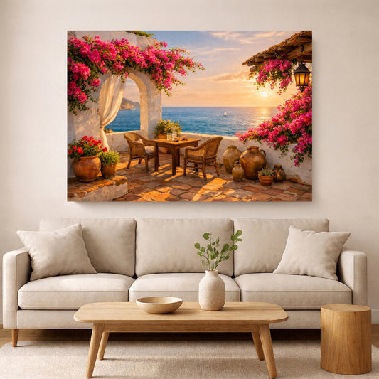 A large rectangular wall art print depicting a Mediterranean seaside patio with pink bougainvillea flowers, a table and chairs, terracotta pots, and a sunset over the ocean, displayed above a light beige sofa in a modern living room.