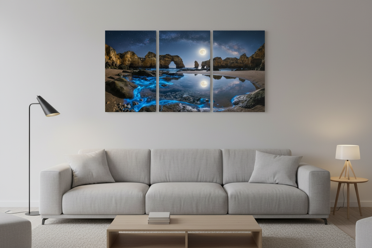Algarve moonlit bioluminescent beach triptych canvas wall art above wide sofa in contemporary living room with grey walls and warm lamp lighting - Portugal Canvas Co